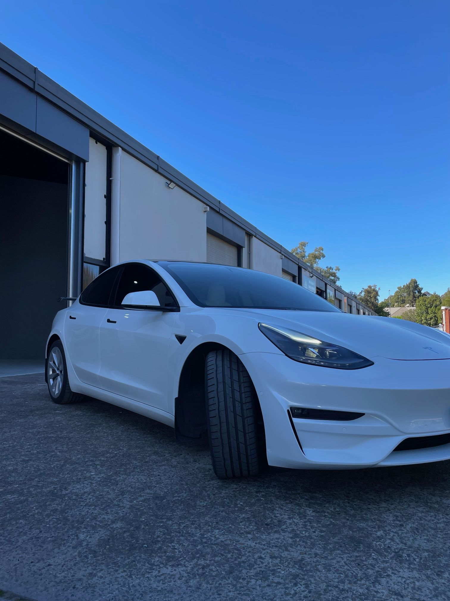 Corner of white Tesla in front of auto shop garage Sydney